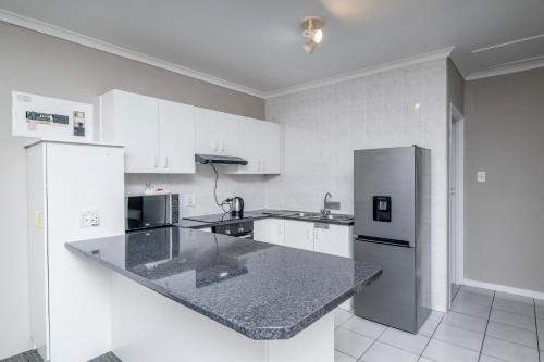 cocina con armarios blancos y encimera de granito en Prime Executive Apartments 2, en Durbanville