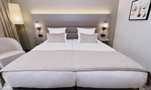 a bedroom with a large white bed and a chair at Leonardo Hotel Hannover in Hannover