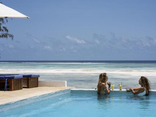 two women sitting in a swimming pool next to the ocean at Nungwi Dreams by Mantis in Nungwi
