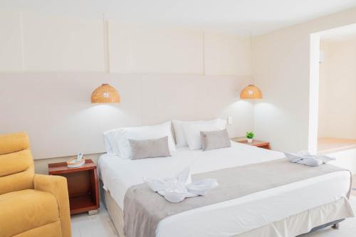 a bedroom with a white bed and a yellow chair at Hotel Playa Palmeras Cartagena - Vía al Mar in Cartagena de Indias