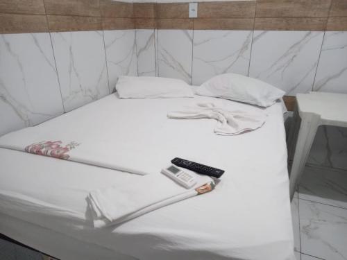 a white bed with a remote control on it at Hotel Contorno in Santa Inês