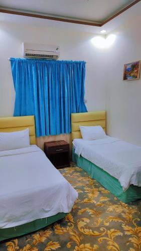 two beds in a room with blue curtains at منتجع سيتي لاند فله رقم 4 in Taif