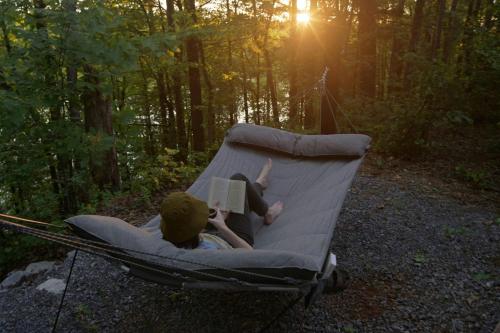 a person laying in a hammock reading a book at Postcard Cabins The Thumb, Outdoor Collection by Marriott Bonvoy in Columbiaville