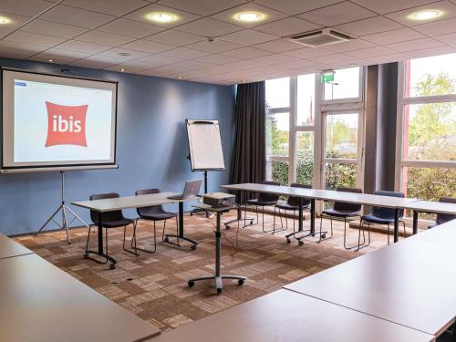 a lecture room with tables and chairs and a screen at ibis Metz Nord in Woippy