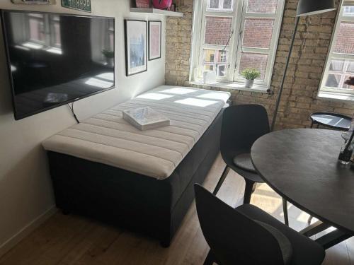 a bed in a room with a table and a flat screen tv at Aalborgs mest centrale lille hyggelige New Yorker lejlighed in Aalborg