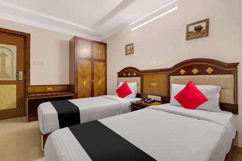 two beds in a hotel room with red pillows at Capital O Elegant Amethyst Business Hotel Near Ragigudda Sri Prasanna Anjaneyaswamy Temple in Bengaluru