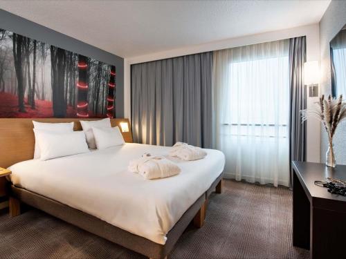 a bedroom with a large white bed with a window at Novotel Paris Est in Bagnolet
