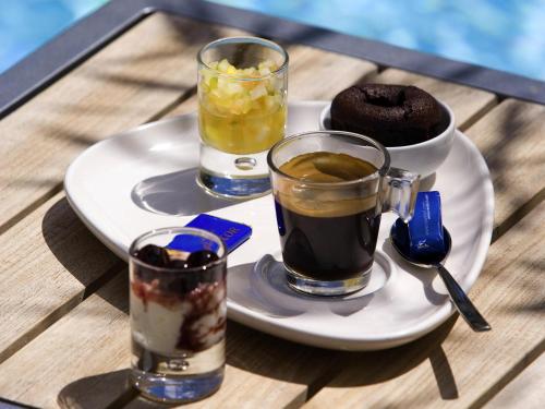 a plate with three drinks on a table with a plate of food at Novotel Paris Nord Expo Aulnay in Aulnay-sous-Bois