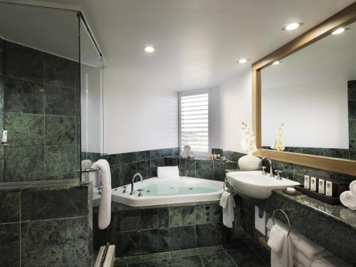 a bathroom with a tub and a sink and a mirror at Sofitel Gold Coast Broadbeach in Gold Coast
