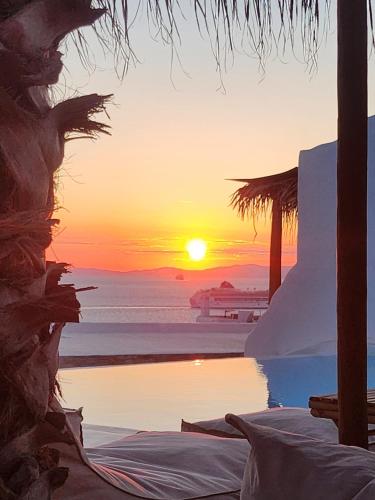 a sunset over a beach with a pool and the ocean at ELLI TROPiCAL LUXURY SUITES SUNSET-INFINITY POOL- SEA SIDE-NEAR CENTER PARKING in Mikonos