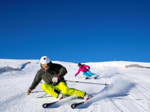 two people are skiing down a snow covered slope at Mountain Chalet Aquarius 5A in Sankt Lorenzen ob Murau