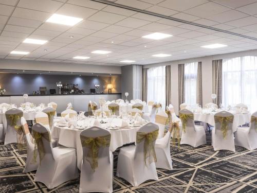 a banquet room with white tables and chairs with bows at Novotel Ipswich Centre in Ipswich