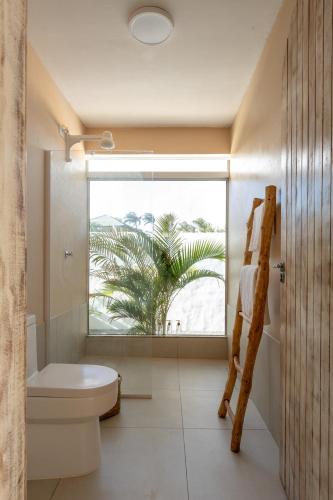 a bathroom with a toilet and a window with a palm tree at Pousada Vila Nazare in São Miguel do Gostoso