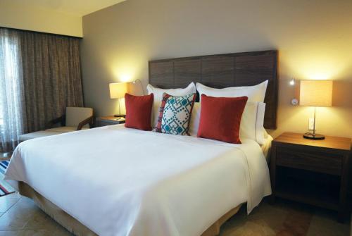 a hotel room with a large white bed with red pillows at Grand Fiesta Americana Los Cabos All Inclusive Golf & Spa in Cabo San Lucas