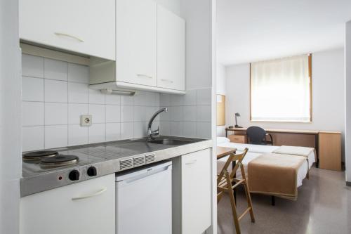 cocina con armarios blancos, fregadero y mesa en Residencia Universitaria Resa Campus de Montilivi, en Girona
