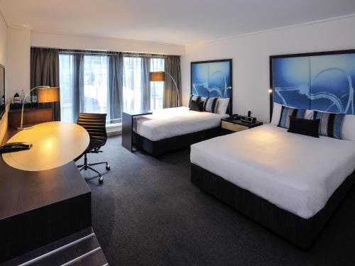 a hotel room with two beds and a desk at Novotel Melbourne On Collins in Melbourne