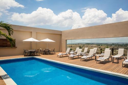 a pool with chairs and tables on a deck at Fiesta Inn Silao Puerto Interior in Silao