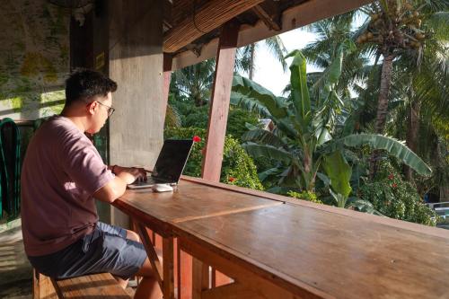 a man sitting at a table with a laptop at Sinag Hostel in General Luna
