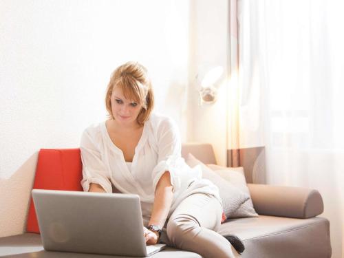 a woman sitting on a couch with a laptop at Novotel Paris Rueil Malmaison in Rueil-Malmaison