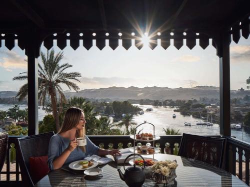 a woman sitting at a table with a cup of coffee at Sofitel Legend Old Cataract in Aswan