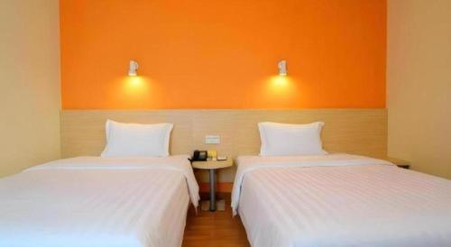 two beds in a room with an orange wall at 7 Days Inn Beijing Shunyi Development Area Mordern Motor City in Beijing