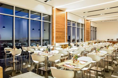 a restaurant with white tables and chairs and large windows at Fiesta Inn Pachuca Gran Patio in Pachuca de Soto