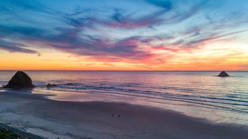 a sunset on a beach with people walking on the sand at Royal Canoe by AvantStay Walk to the Shore Private Yard in Arch Cape