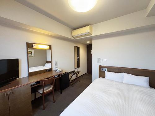 a hotel room with a bed and a desk and a mirror at Route Inn Grantia Himi Wakuranoyado in Himi