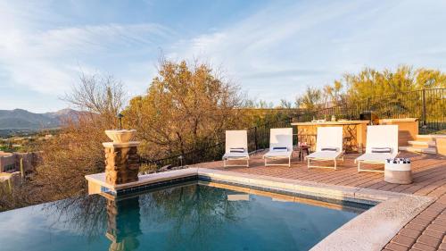 a swimming pool with chairs and a table at Sunbeam by AvantStay Elegant Private Desert Home w Infinity Pool Spa View in Cave Creek