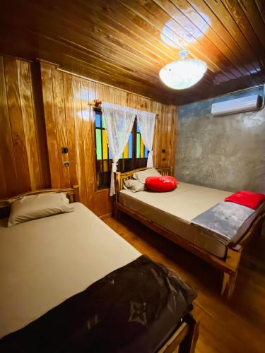 two beds in a room with wooden walls and windows at เรือนบรรเจิดโฮมสเตย์ in Ban Nok
