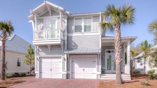 a white house with two garage doors and palm trees at Coconut Cove by AvantStay Deck w Hot Tub Access to 2 Pools in Santa Rosa Beach