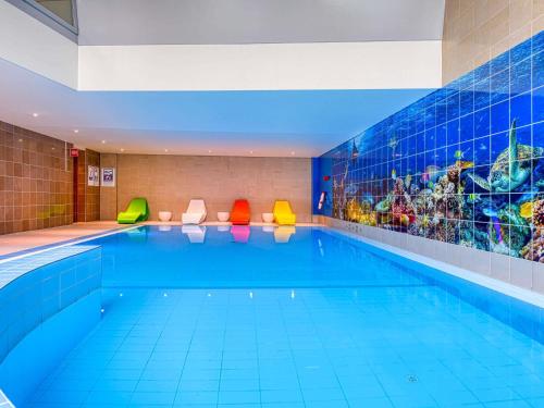 a large swimming pool with colorful chairs in a building at Novotel Zurich City West in Zürich