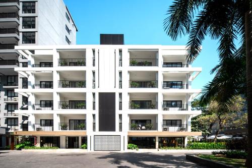 a white apartment building with palm trees in front of it at Floral Court Hotel & Residence Sukhumvit 13 in Bangkok