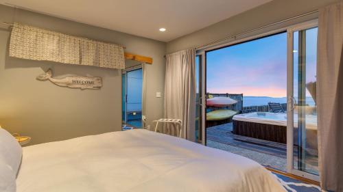 a bedroom with a bed and a balcony with a view at Chic Whidbey Island Waterfront Home w Hot Tub Firepits Views in Coupeville