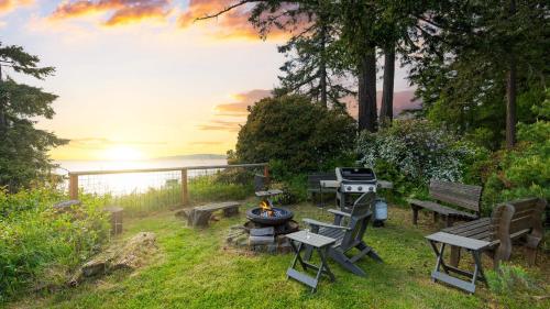 a grill and picnic tables in a yard with the sunset at Maxwelton Aerie Bluffside Retreat w Sweeping Puget Sound Views Firepit in Clinton
