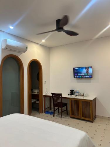 a bedroom with a bed and a desk and a ceiling fan at Vang Anh Homestay Hoi An in Hoi An