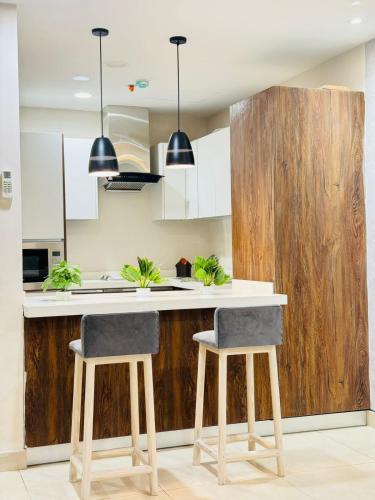 a kitchen with white cabinets and a counter with two stools at Gold Crest Luxury Serviced Apartments City View DHA Lahore in Lahore