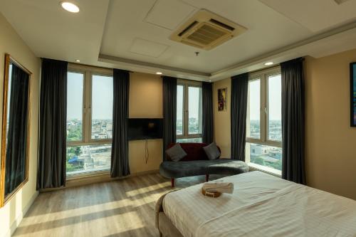 a bedroom with a bed and a chair and windows at Gold Crest Luxury Serviced Apartments City View DHA Lahore in Lahore
