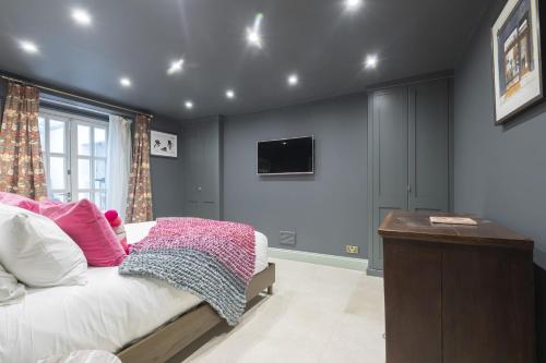 a bedroom with a bed with pink pillows and a tv at Luxury 4-Bed Regency Townhouse Overlooking Montpellier Gardens in Cheltenham