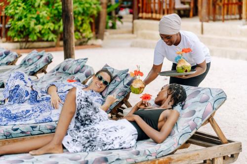 a man serving two women in beds on a beach at Shanuo Beach Bungalows in Michamvi