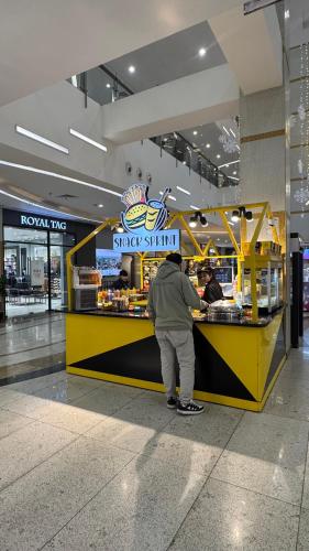 a man standing at a counter in a shopping mall at Gold Crest Grand Executive Hotel Apartments DHA Lahore in Lahore