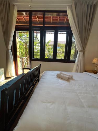 a bedroom with a large white bed with windows at Vang Anh Homestay Hoi An in Hoi An
