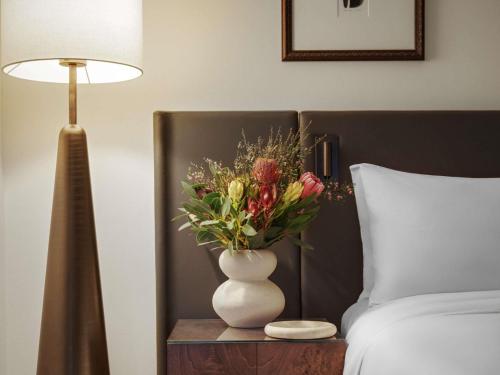 a vase of flowers on a table next to a bed at Sofitel Sydney Wentworth in Sydney