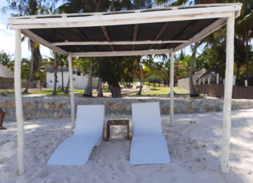 a pavilion with two chairs and a table in the sand at Giraffe House Vilankulo in Vilanculos