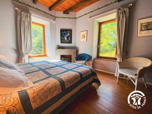 a bedroom with a bed and two chairs and two windows at Le Moulin du Go in Tauriac-de-Naucelle