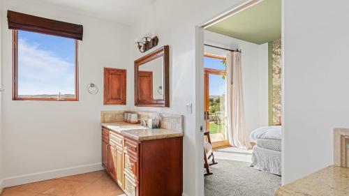 a bathroom with a sink and a mirror and a bedroom at Wine Country Escape w Views Wine Cellar Gym Caterina Dusi Vineyard by AvantStay in Paso Robles