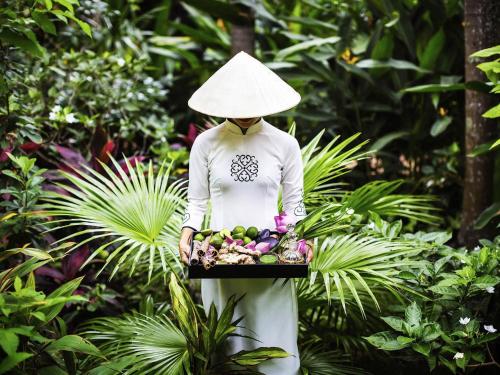 a woman wearing a conical hat holding a tray of fruit at La Veranda Resort Phu Quoc - MGallery in Phu Quoc
