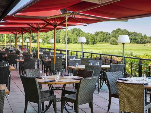 a restaurant with tables and chairs with a view of a golf course at Cabot Hotel Bordeaux - MGallery Collection in Le Pian-Médoc