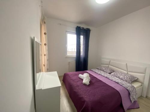 a bedroom with a bed with purple sheets and a window at Fushë Kosova Apartment in Kosovo Polje