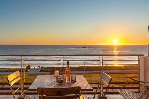 a table with a bottle of wine on a balcony with the sunset at Eden on The Bay 250 in Bloubergstrand